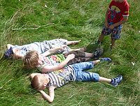 Drei Kinder liegen im Gras, und ein viertes Kind steht daneben.