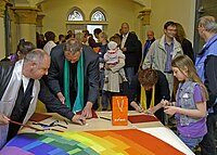 Menschen schreiben auf einem großen regenbogenfarbenen Banner.